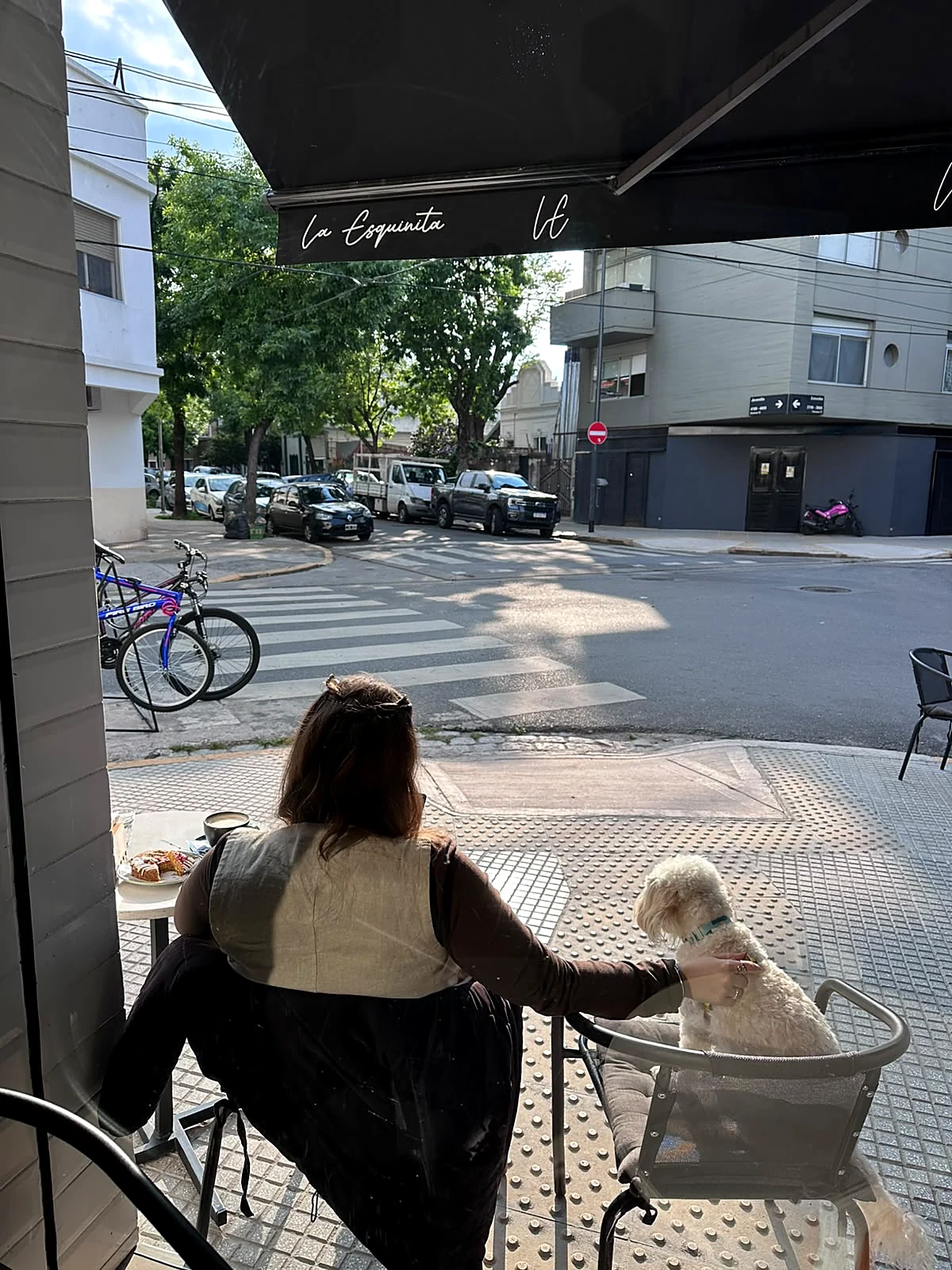 Una vecina toma café en la vereda con su perro sentado en la silla de al lado